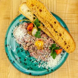 Delicious beef tartare plated with cheese, tomato, and crispy bread on a turquoise dish.