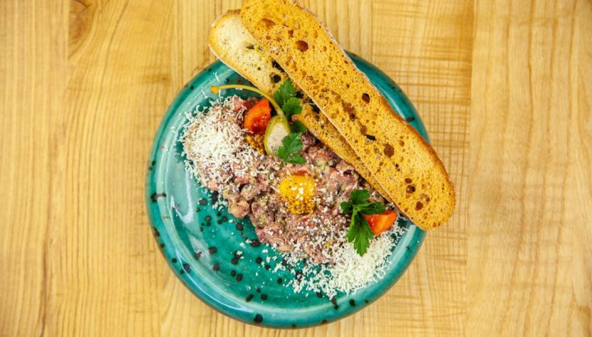 Delicious beef tartare plated with cheese, tomato, and crispy bread on a turquoise dish.