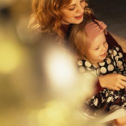 Tender moment between mother and daughter decorating a festive Christmas tree.