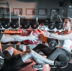 A couple engaged in a fitness session using a medicine ball in a gym environment.