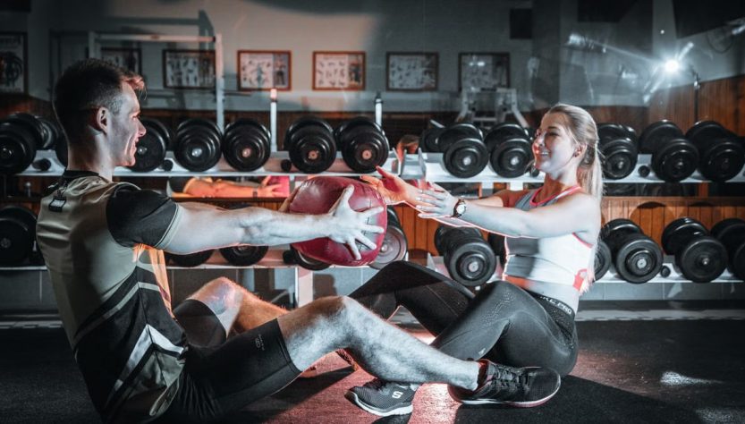 A couple engaged in a fitness session using a medicine ball in a gym environment.